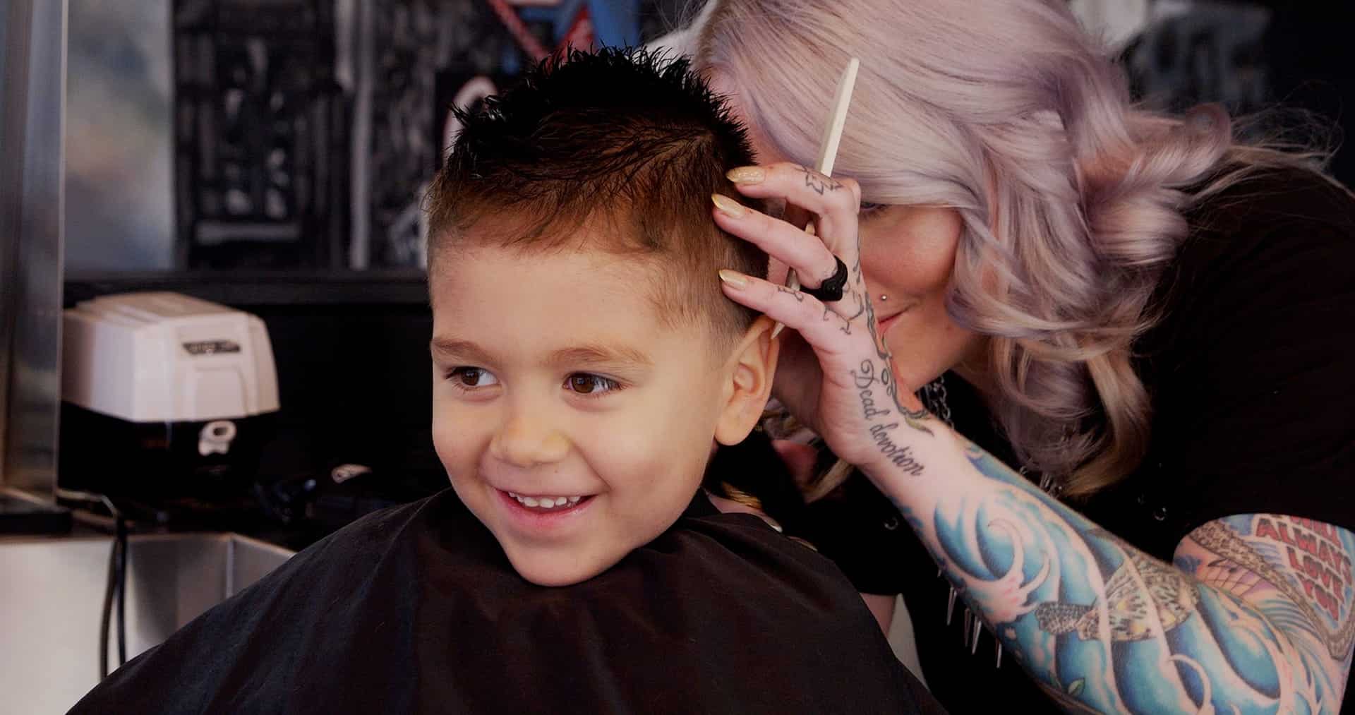 A smiling young boy getting a taper fade haircut for Back to School from Floyd's Barbershop.