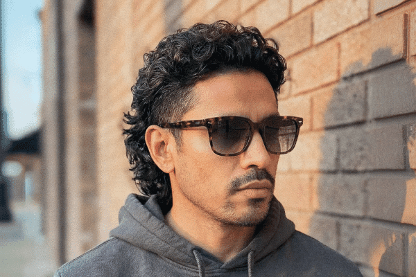 A young man wearing sunglasses with a curly modern mullet cut by Floyds Barbershop