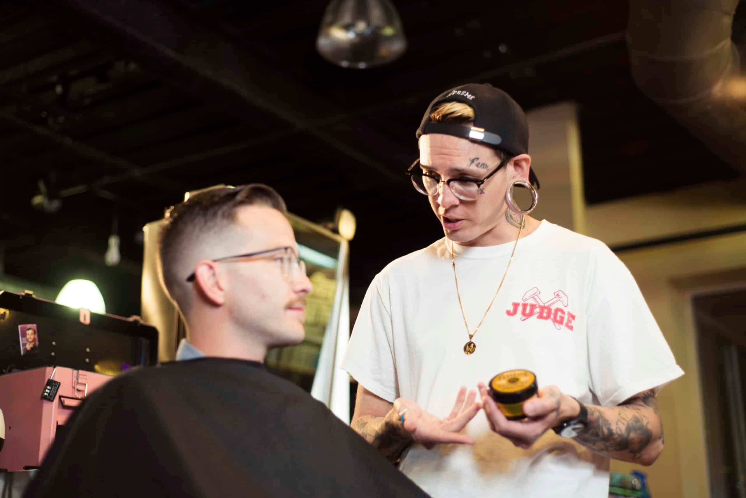 A Floyd's 99 Barber holding a Professional Hair Styling product, teaching the client how to use